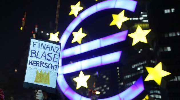 A woman holds a sign in front of the Euro currency sign next to the European Central Bank headquarters during a demonstration against the Euro Finance Week in Frankfurt